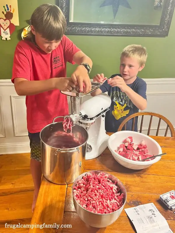 2 boys putting brisket into a meat grinder