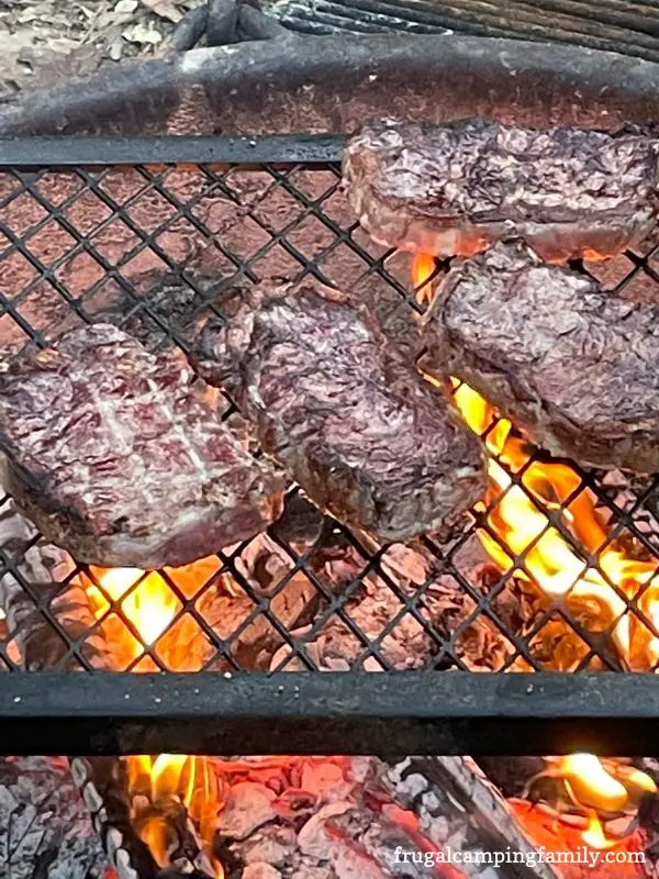 grilling steaks over a campfire